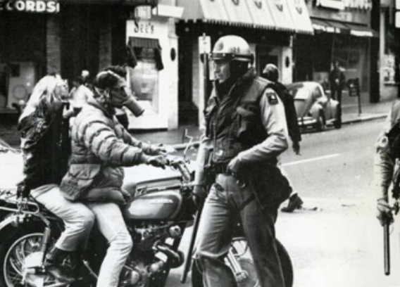 Photo of people in gas masks on motorcycle being approached by armed police 